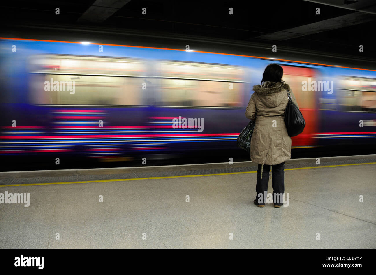 Donna in piedi da solo sulla piattaforma della stazione con il treno in movimento al di là Foto Stock