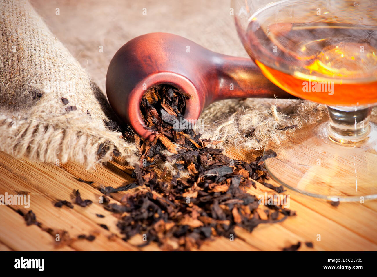 Bicchiere di cognac e il tubo con il tabacco sul tavolo di legno con tela di lino Foto Stock