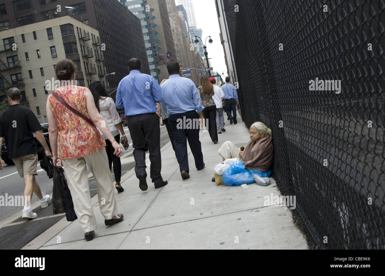 Senzatetto anziani donna seduta sul marciapiede lungo la 8th Avenue a New York come il mondo passa con la sua. Foto Stock