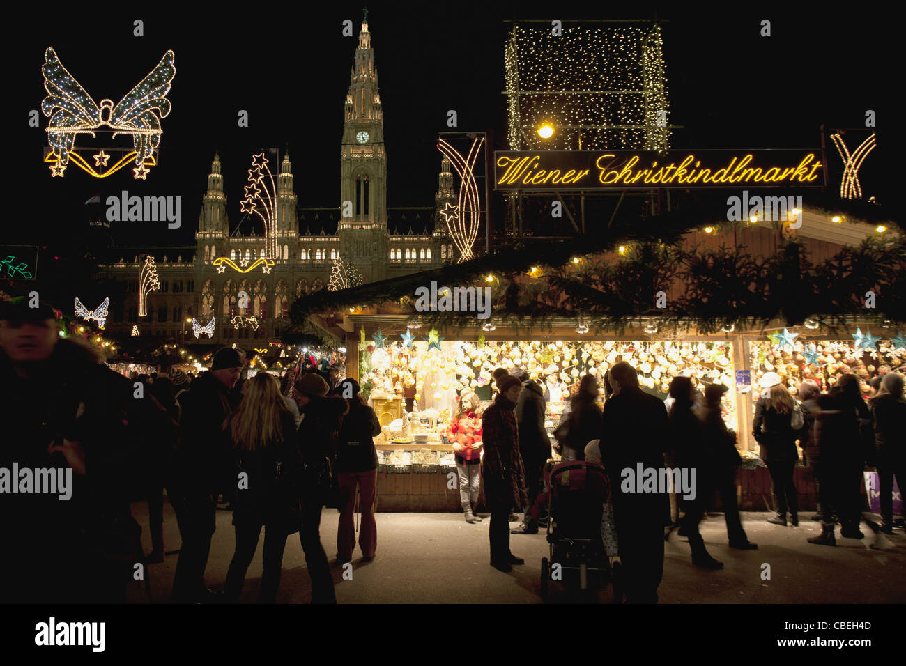 Le luci di Natale illuminano il cielo notturno come le persone si radunano alla Wiener Christkindlmarkt, a Vienna Town Hall in Austria. Foto Stock