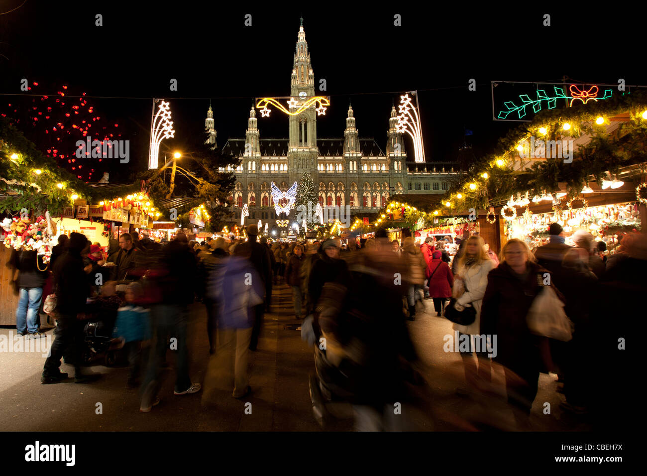 Le luci di Natale illuminano il cielo notturno come le persone si radunano alla Wiener Christkindlmarkt, a Vienna Town Hall in Austria. Foto Stock