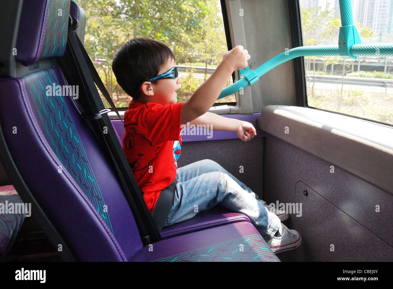 Si tratta di un bambino ragazzo che finge di guidare un autobus con double deck. Egli indossa t-shirt rossa e occhiali da sole. Egli è solo e in jeans. Foto Stock