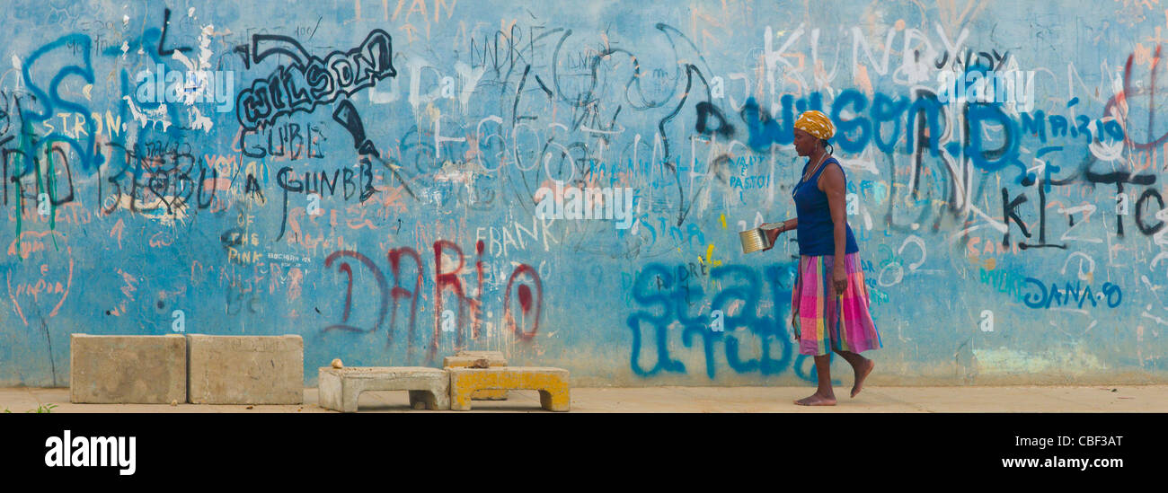 Donna passando da una parete coperta di graffiti, Benguela, Angola Foto Stock