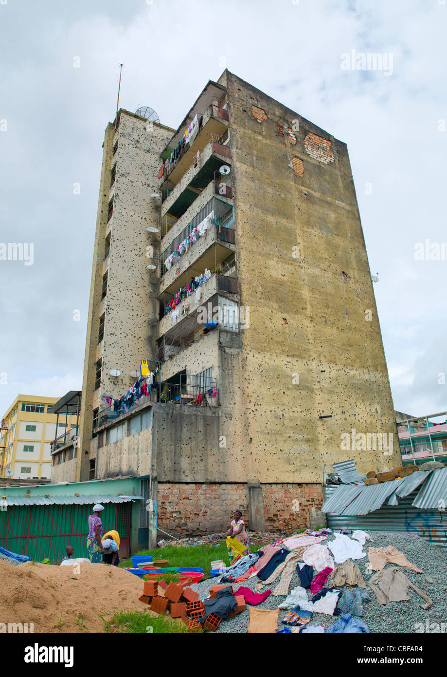 Donne che svolgono il loro servizio lavanderia al fondo del loro edificio riddled con Bullet gli impatti dalla guerra civile, Huambo, in Angola Foto Stock