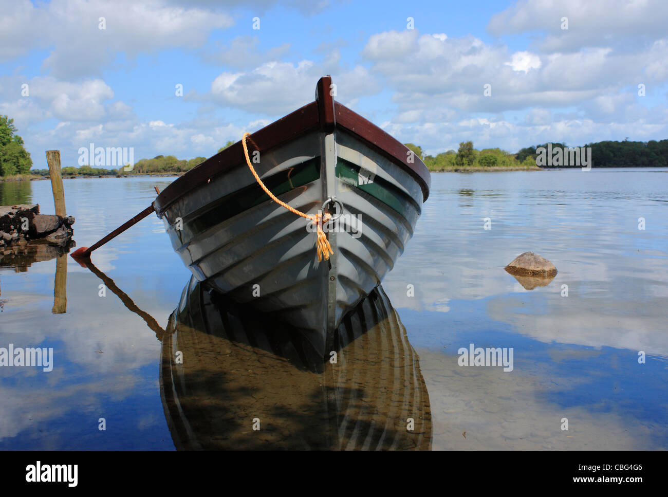 Una barca a remi si trova in un tranquillo lago irlandese che riflette lo scafo della barca al fianco di un blu luminoso giorno di estate in Irlanda. Foto Stock