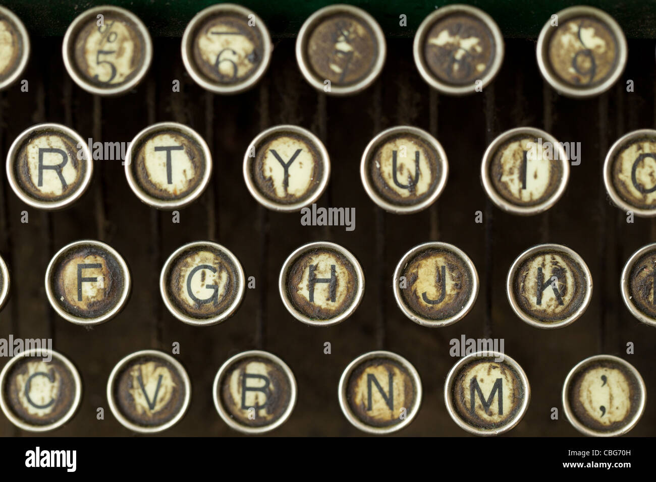 Vista ravvicinata di una fila di chiavi da scrivere circolari metalliche che mostrano segni di usura ed età. I tasti visualizzano le lettere (R, T, Y, U, i, O, F, G, H, J, K, C, V, B, N, m) e numeri (5, 6, 7, 8, 9) Foto Stock