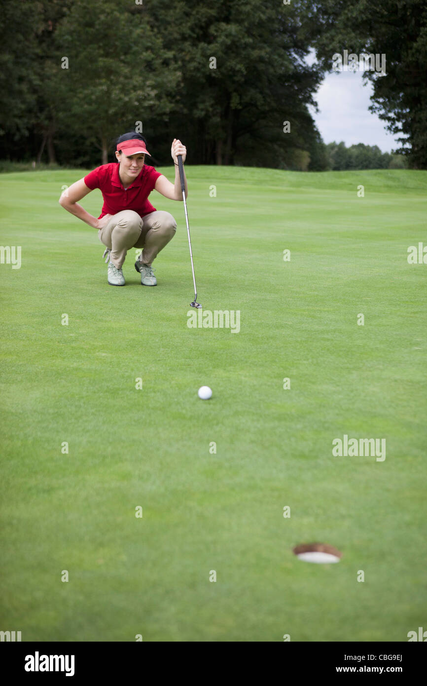 Un giocatore di golf femminile accovacciato studiando la distanza del foro Foto Stock