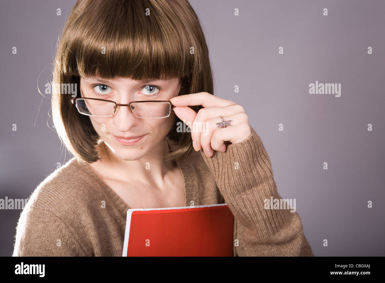 Una giovane donna (insegnante o studente) guardando da dietro gli occhiali. Un file di rosso nelle sue mani Foto Stock