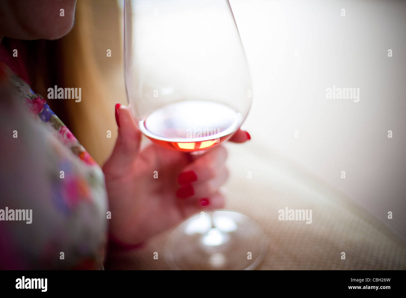 Donna che mantiene un bicchiere di vino rosato. Sun è riflessa dal vetro e vino. Foto Stock