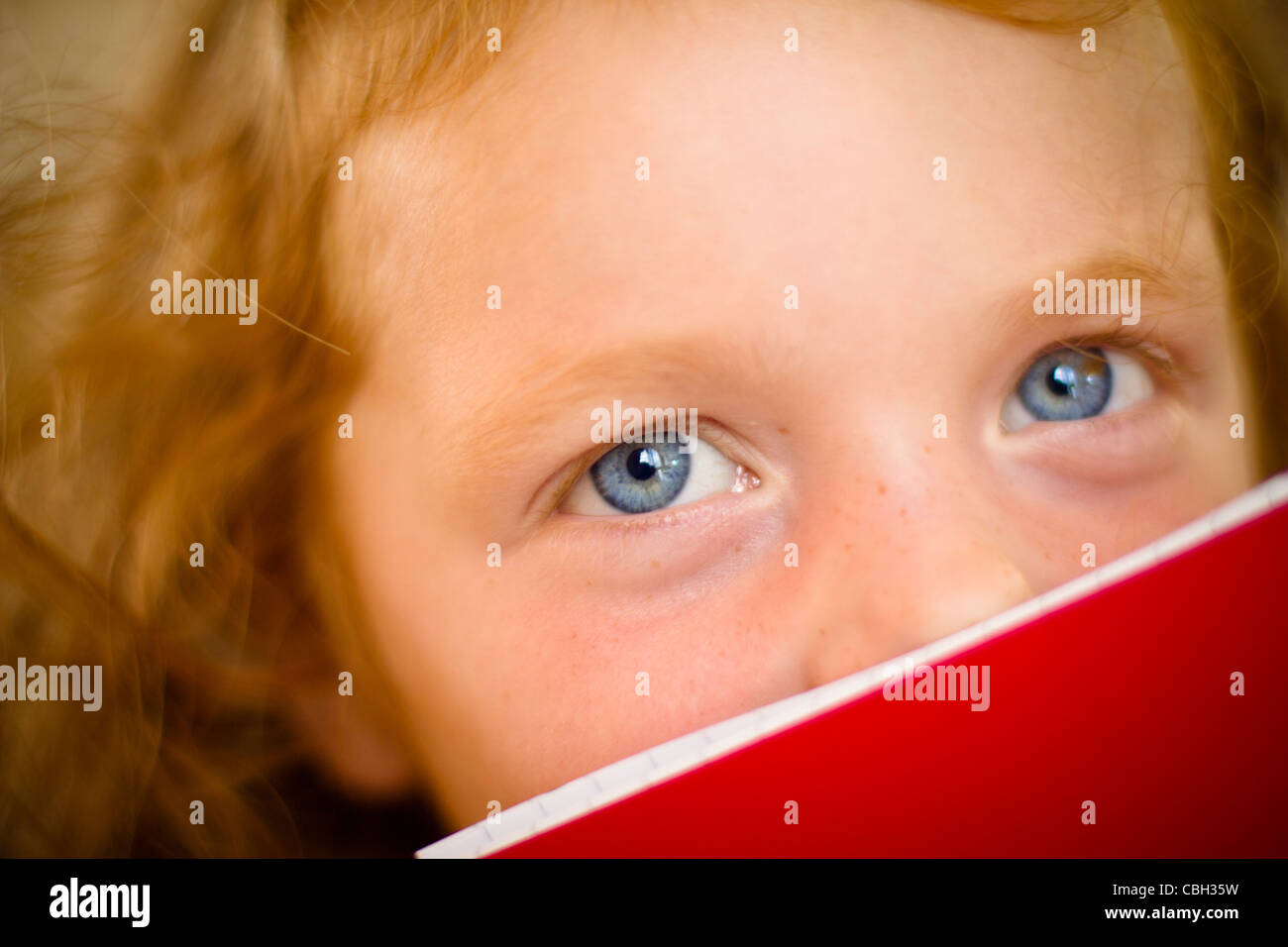 Bambina, di età compresa tra i 5, il peering sopra la parte superiore del suo libro. Foto Stock