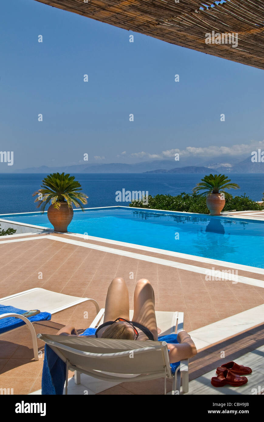Donna rilassarsi sui lettini prendisole con lusso piscina infinity e costiere eccezionale vista sul mare dietro Foto Stock