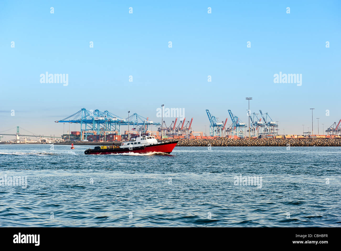 Una alimentazione trasporto barca si muove attraverso un porto commerciale con la gru e attrezzature pesanti sistemi in background. Foto Stock