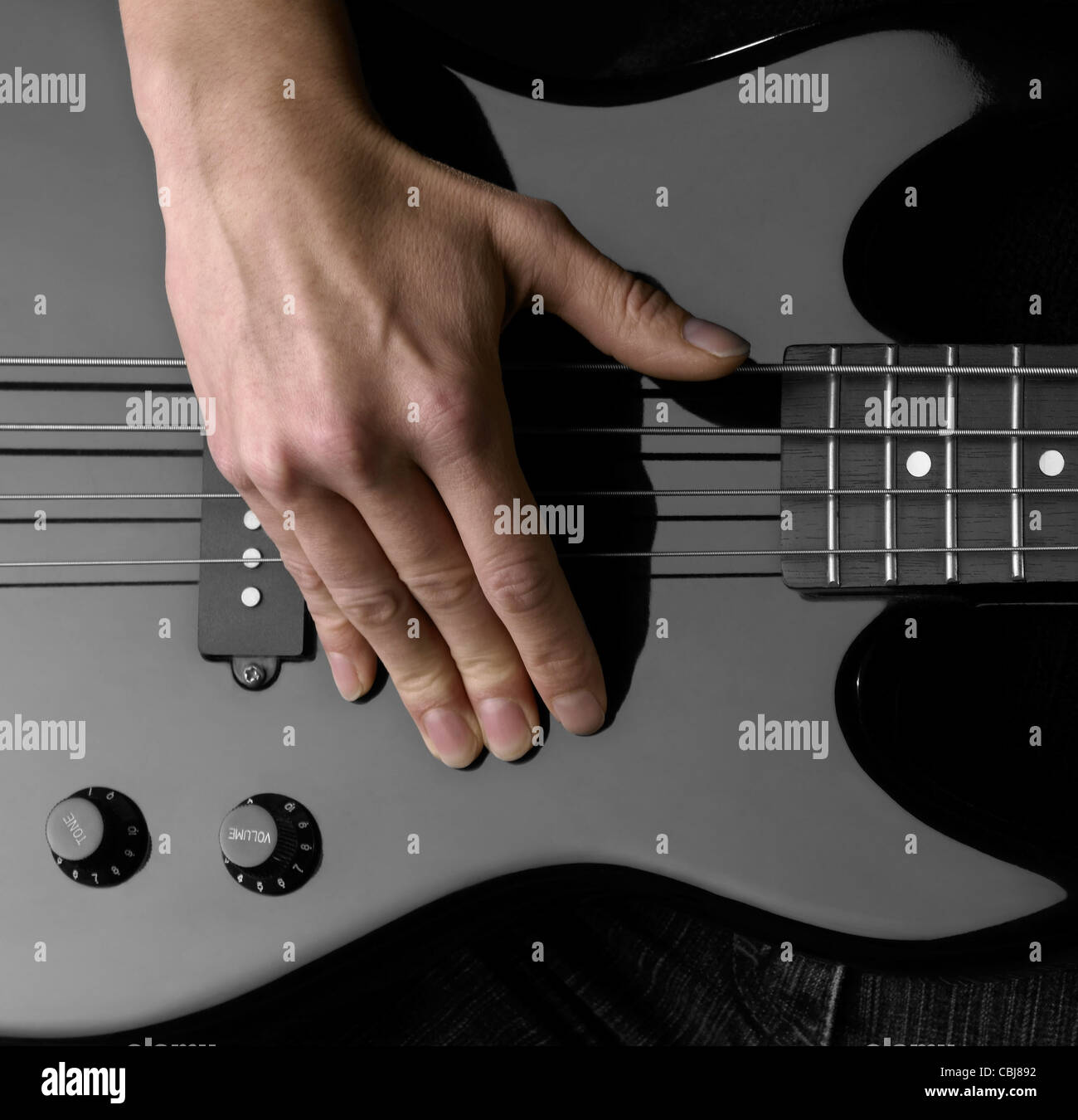 Mano femmina sul dettaglio di un black bass guitar in dark indietro Foto Stock