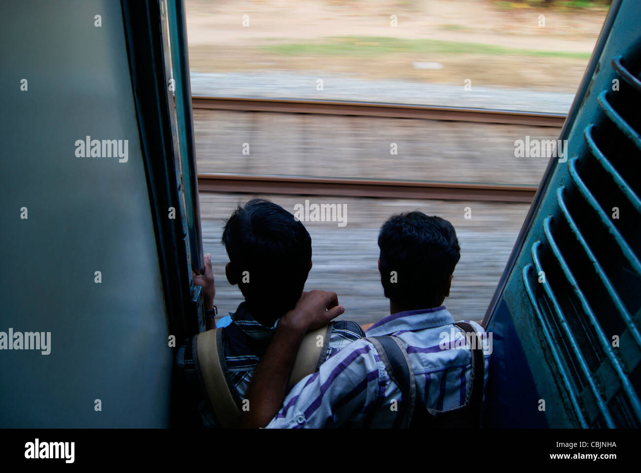 Due giovani amici seduti pericolosamente in un rapido movimento del treno illegalmente nelle fasi di disco metallico di ingresso della porta Foto Stock