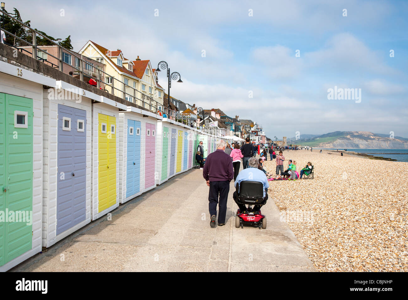 Le persone di fronte alla spiaggia a piedi in Lyme Regis Dorset, Regno Unito, con persona su scooter disabili Foto Stock