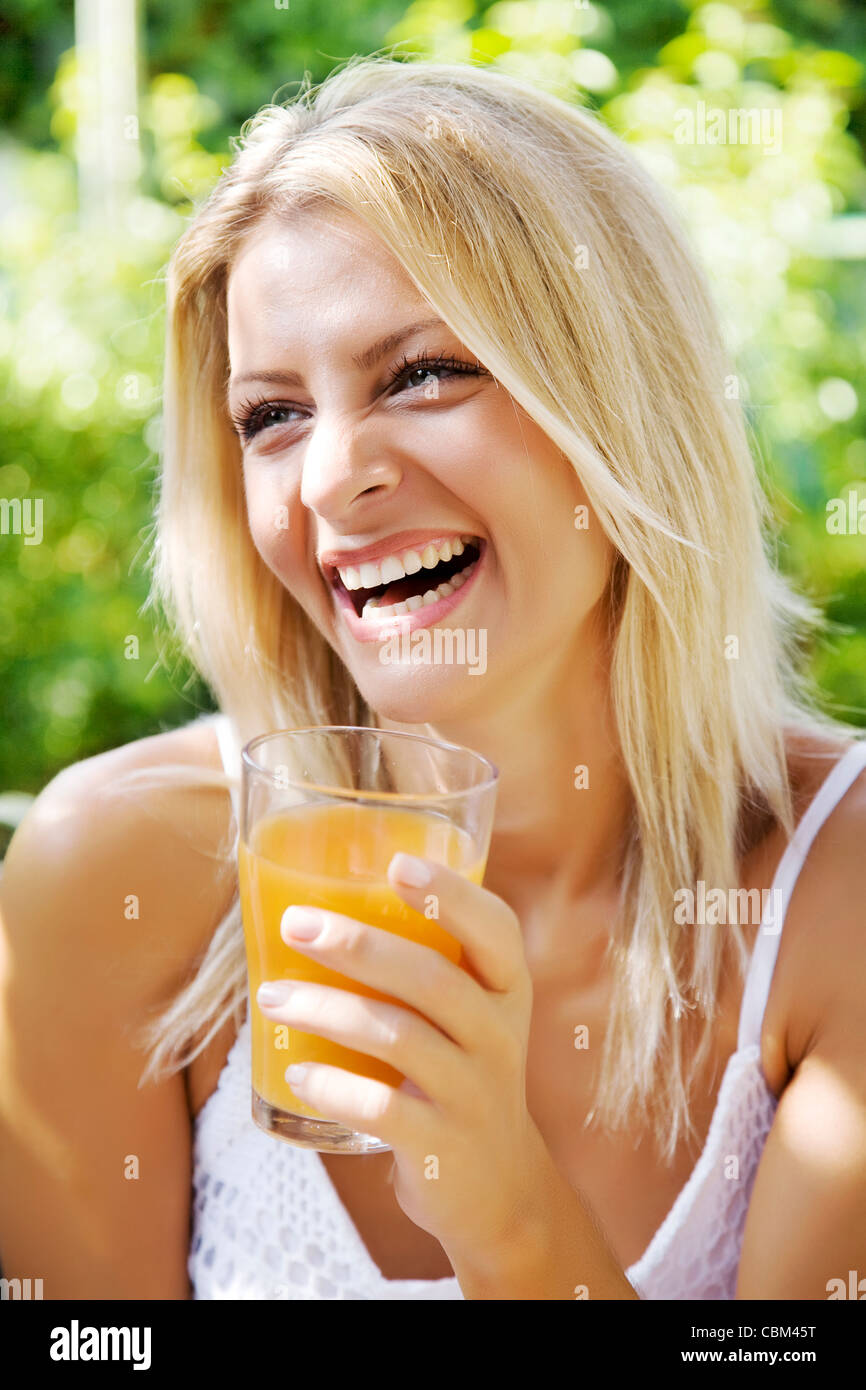 Donna felice di bere il suo mattina succo di arancia nel suo giardino Foto Stock