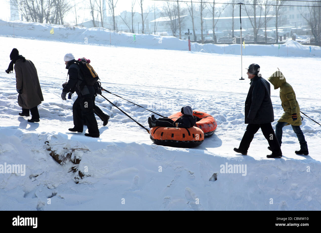 Tirando i ragazzi attraverso la neve in galleggianti gonfiabili, Harbin, Cina Foto Stock