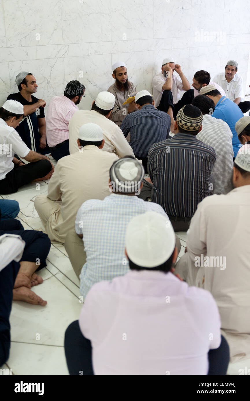 Uomo di lettura da un islamico di prenotare per un gruppo di visitatori nella sala di preghiera della moschea di Kowloon Foto Stock