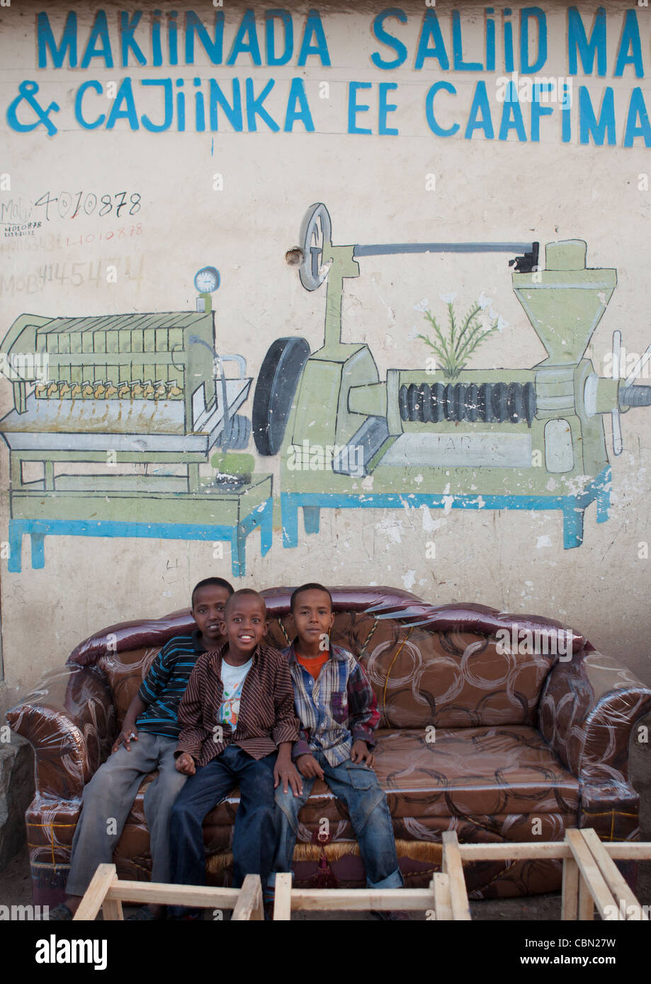 Tre bambini seduti in divano sotto la pubblicità per la fabbrica, Hargeisa Somaliland Foto Stock