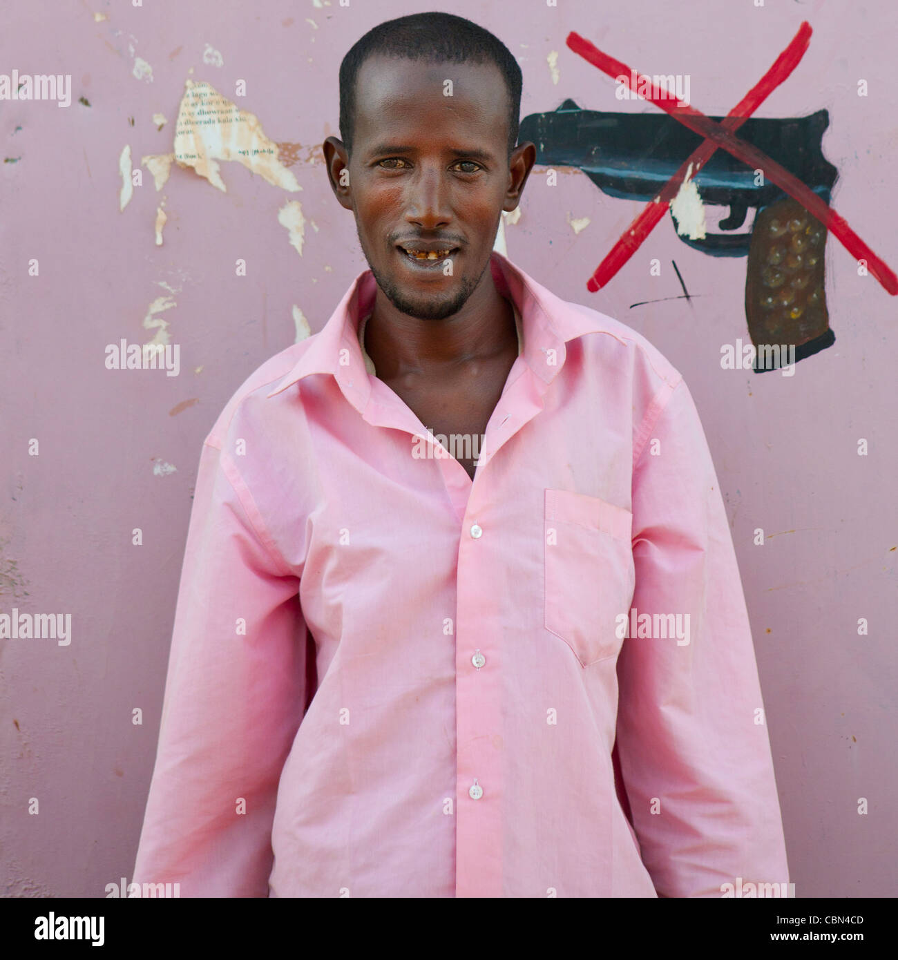 Anti arma segno dipinto sul muro, giovane adulto in maglia rosa in piedi contro la parete Burao Somaliland Foto Stock
