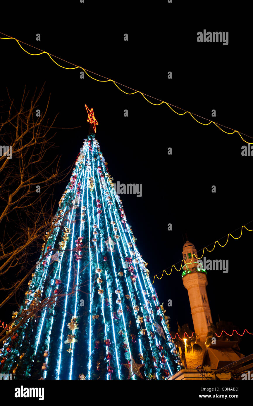 L'accensione di un albero di Natale domina Piazza della Mangiatoia e una vicina moschea in Cisgiordania città di Betlemme. Foto Stock