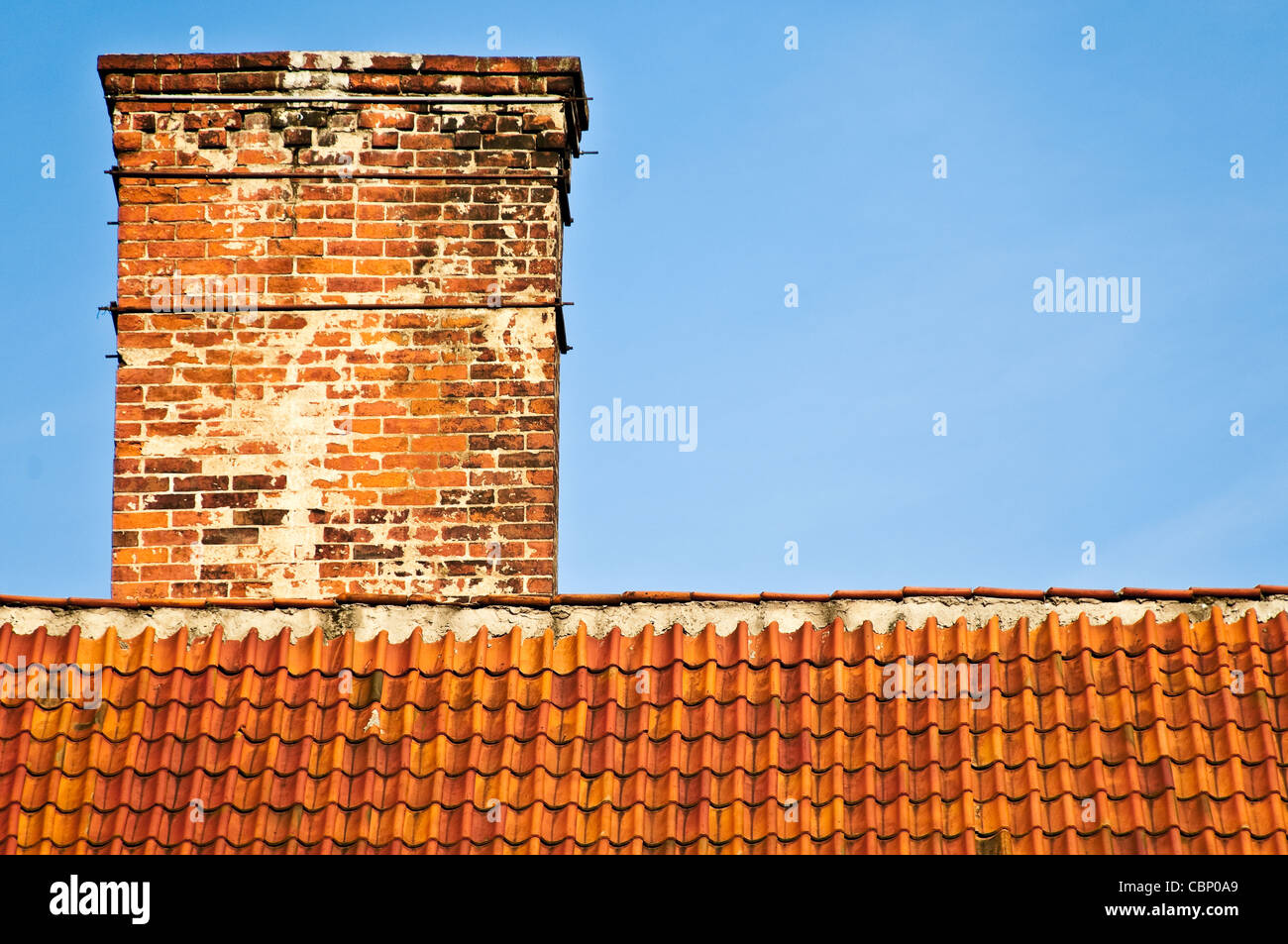 Rosso e arancione in alto sul tetto della vecchia casa in mattoni con camino e cielo blu in background Foto Stock