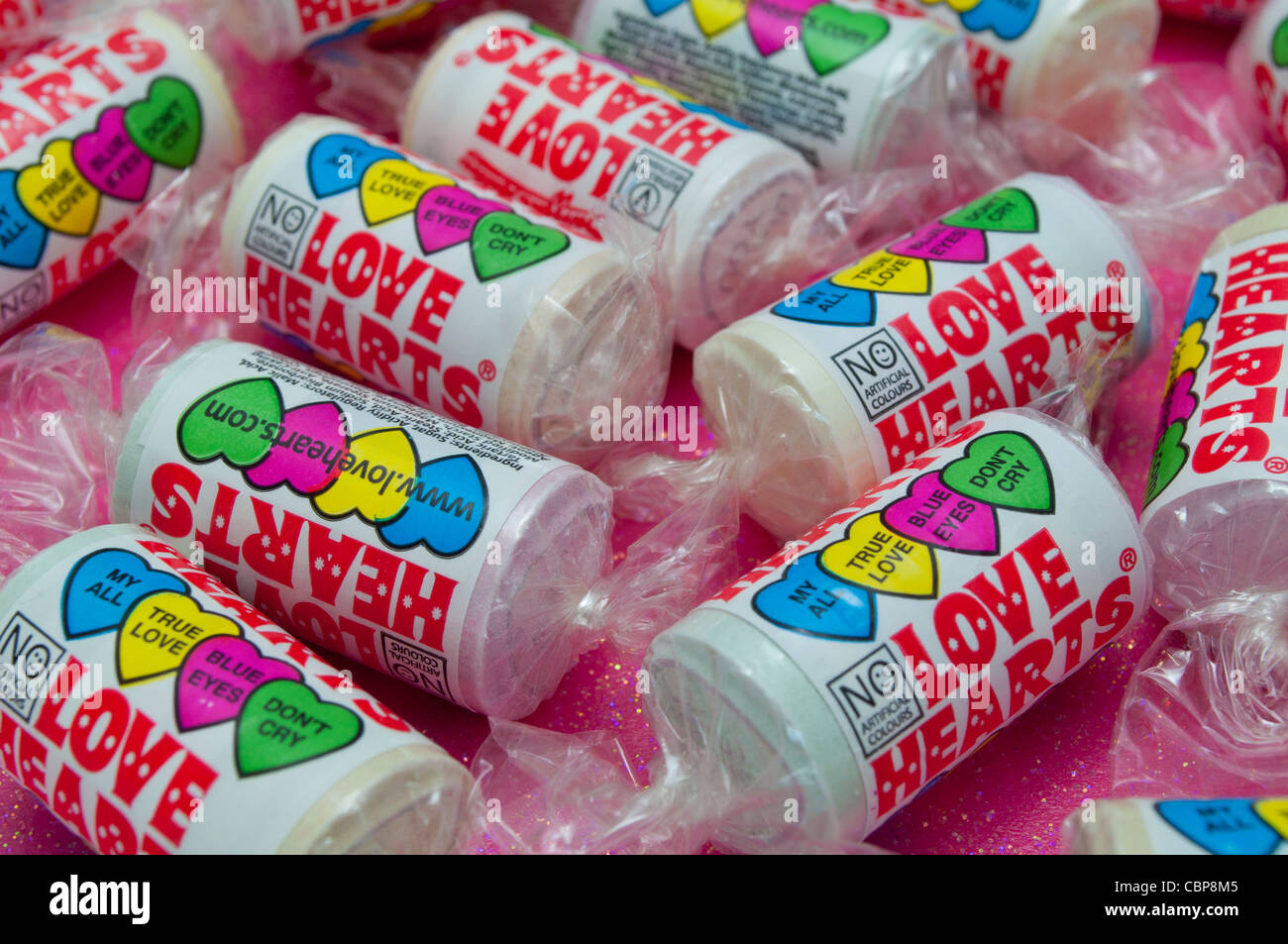 Close up di tubi di amore del cuore dolci caramelle su un vivace sfondo rosa con messa a fuoco selettiva Foto Stock
