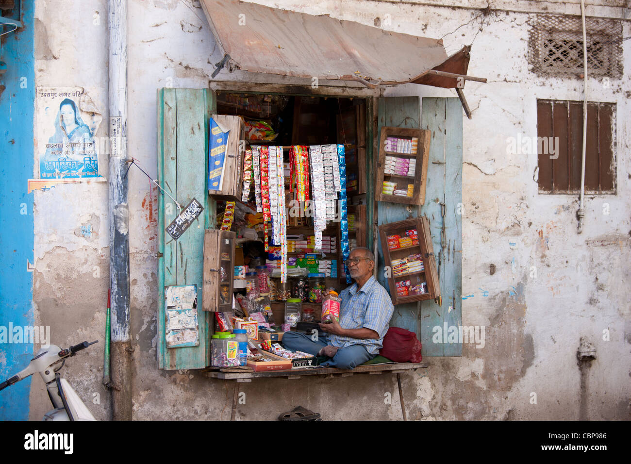 Stallholder vendono dolci, tabacco e prodotti alimentari si siede nella finestra del negozio nella città vecchia in Udaipur, Rajasthan, stato dell India occidentale Foto Stock