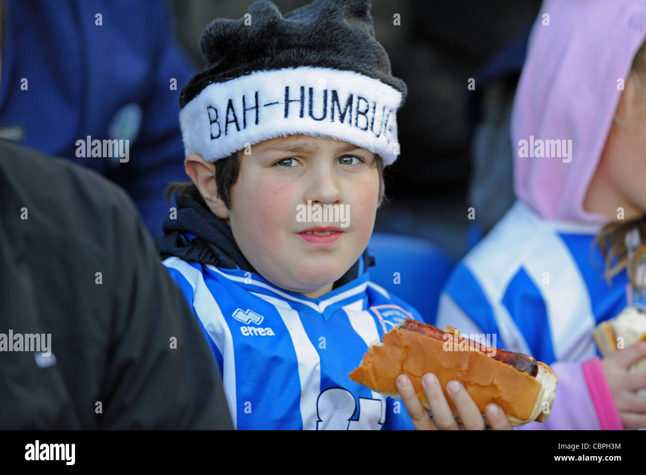 Giovane che mangia un cane caldo che indossa un cappello di Natale Bah-Humbug Alla partita di calcio di Brighton UK Foto Stock