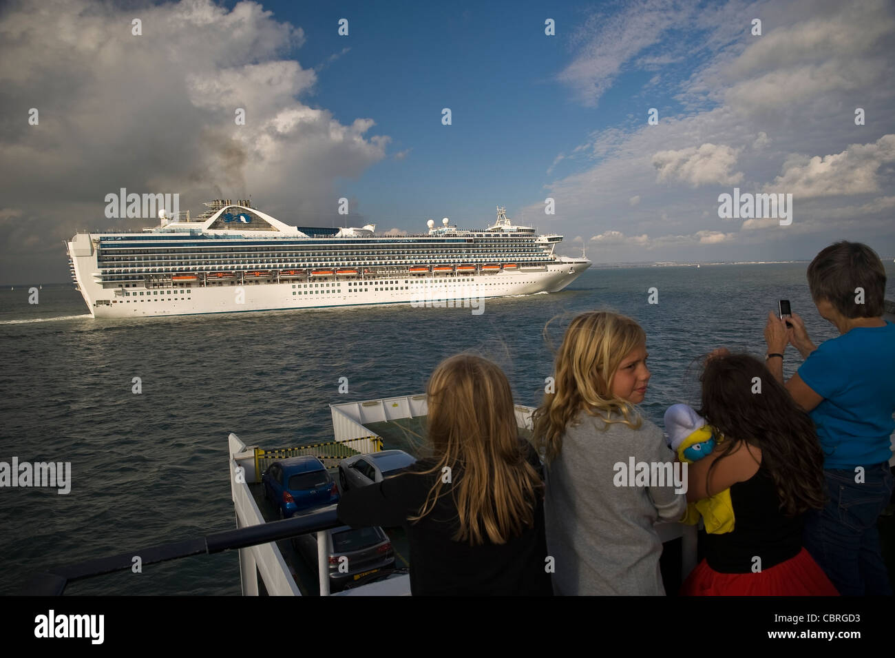 I passeggeri su un isola di Wight traghetto per auto la visione di una grande nave da crociera passano sul Solent vicino a Southampton, Regno Unito Foto Stock
