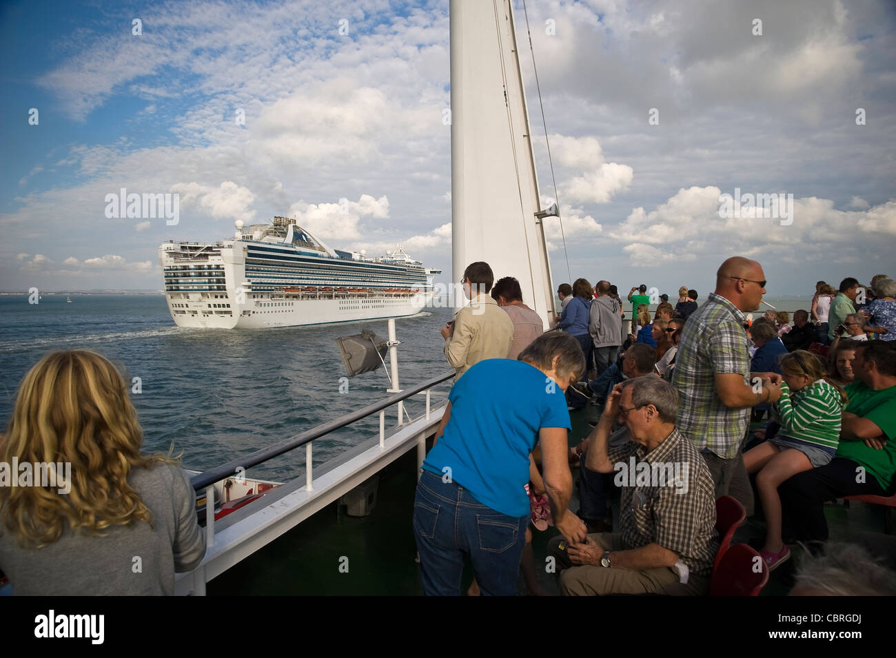 I passeggeri su un isola di Wight traghetto per auto la visione di una grande nave da crociera passano sul Solent vicino a Southampton, Regno Unito Foto Stock