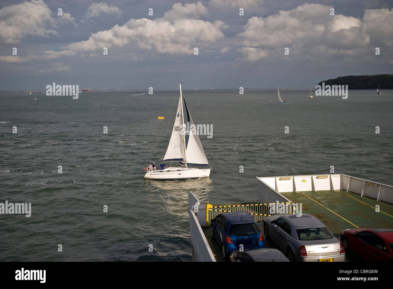 Un piccolo yacht vele attraverso la prua di un isola di Wight traghetto per auto sul Solent, Hampshire, Regno Unito Foto Stock