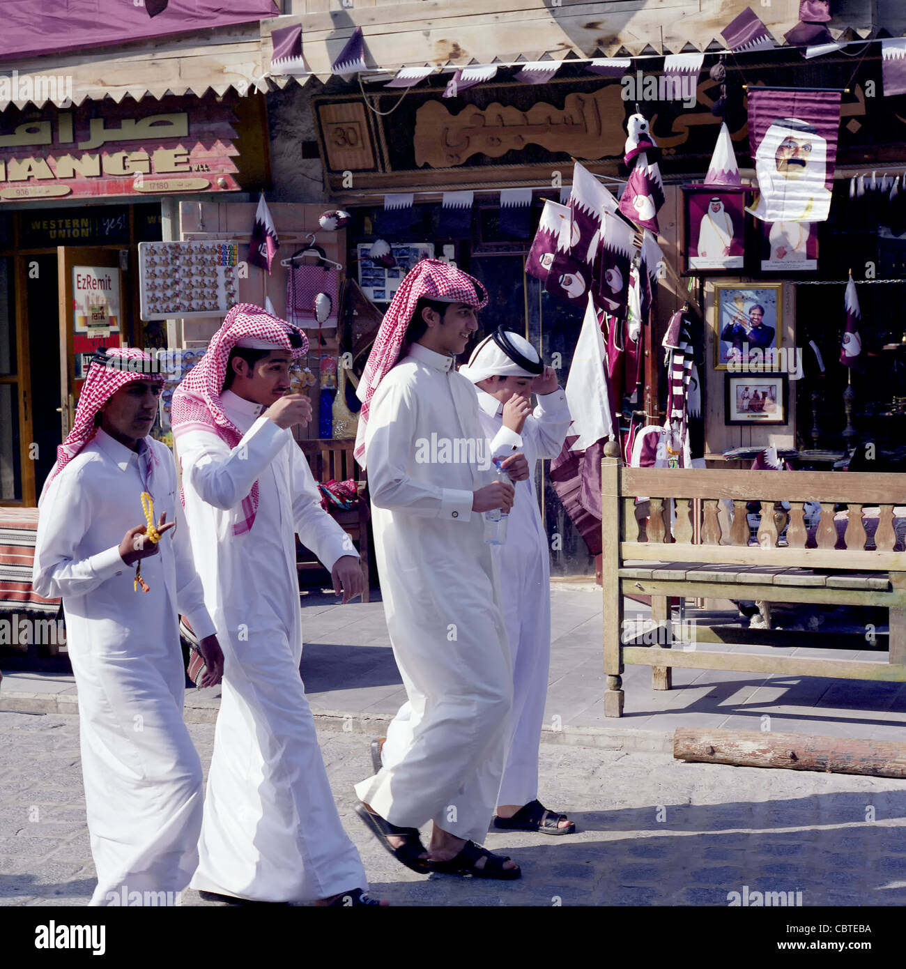 Quattro Qataris a piedi passato un negozio che mostra le bandiere nazionali e le foto del Emiro e erede apparenti appena prima Giornata Nazionale nel 2011 Foto Stock