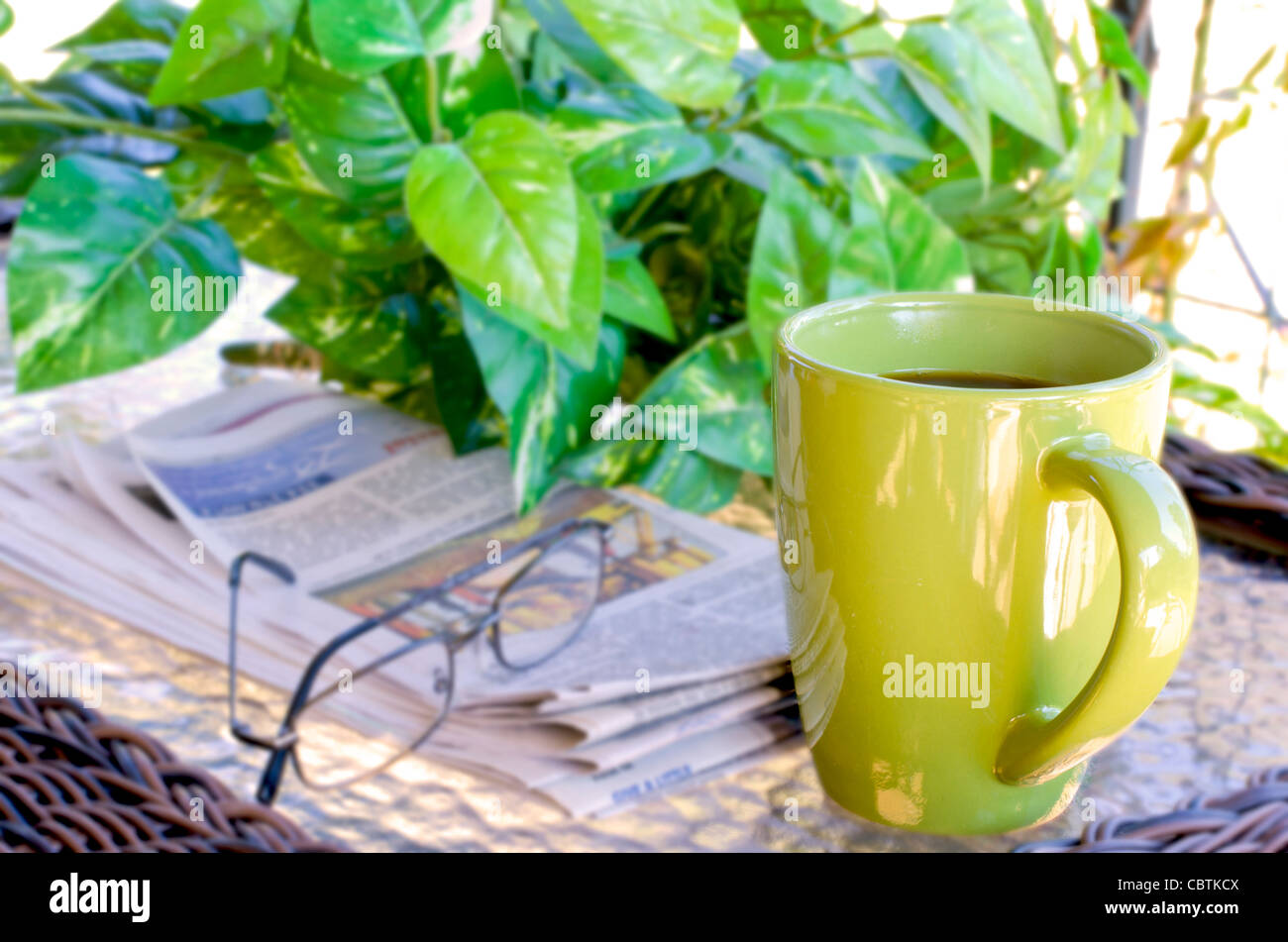 Il caffè del mattino con i giornali e gli occhiali da lettura. Pianta verde in background. Foto Stock