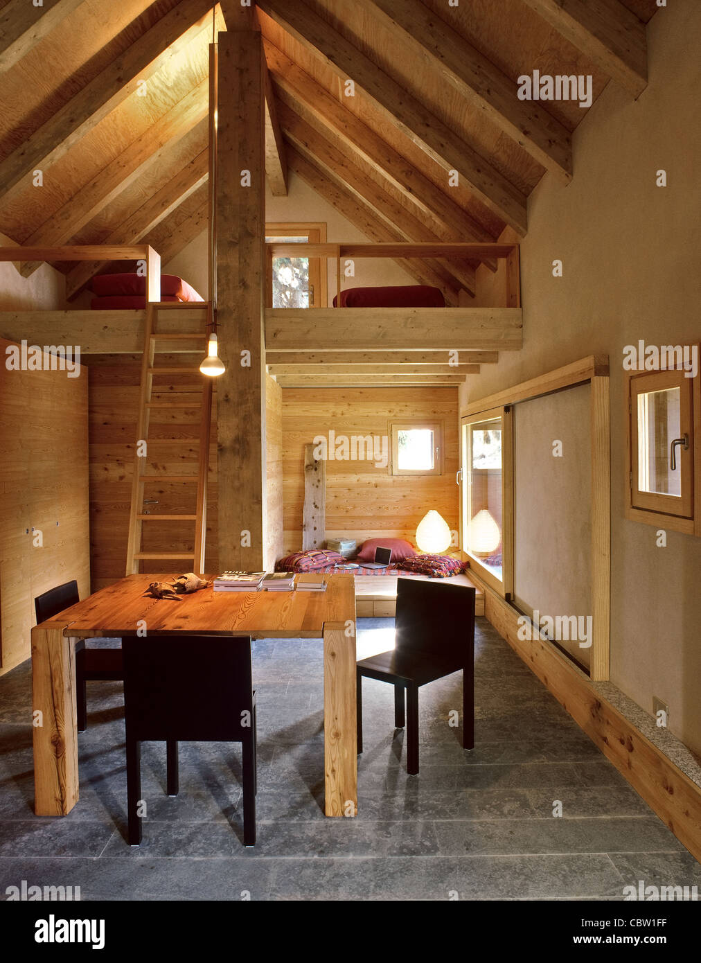 Interno del chalet con tavolo da pranzo e soppalco, pavimento in pietra e legno Foto Stock