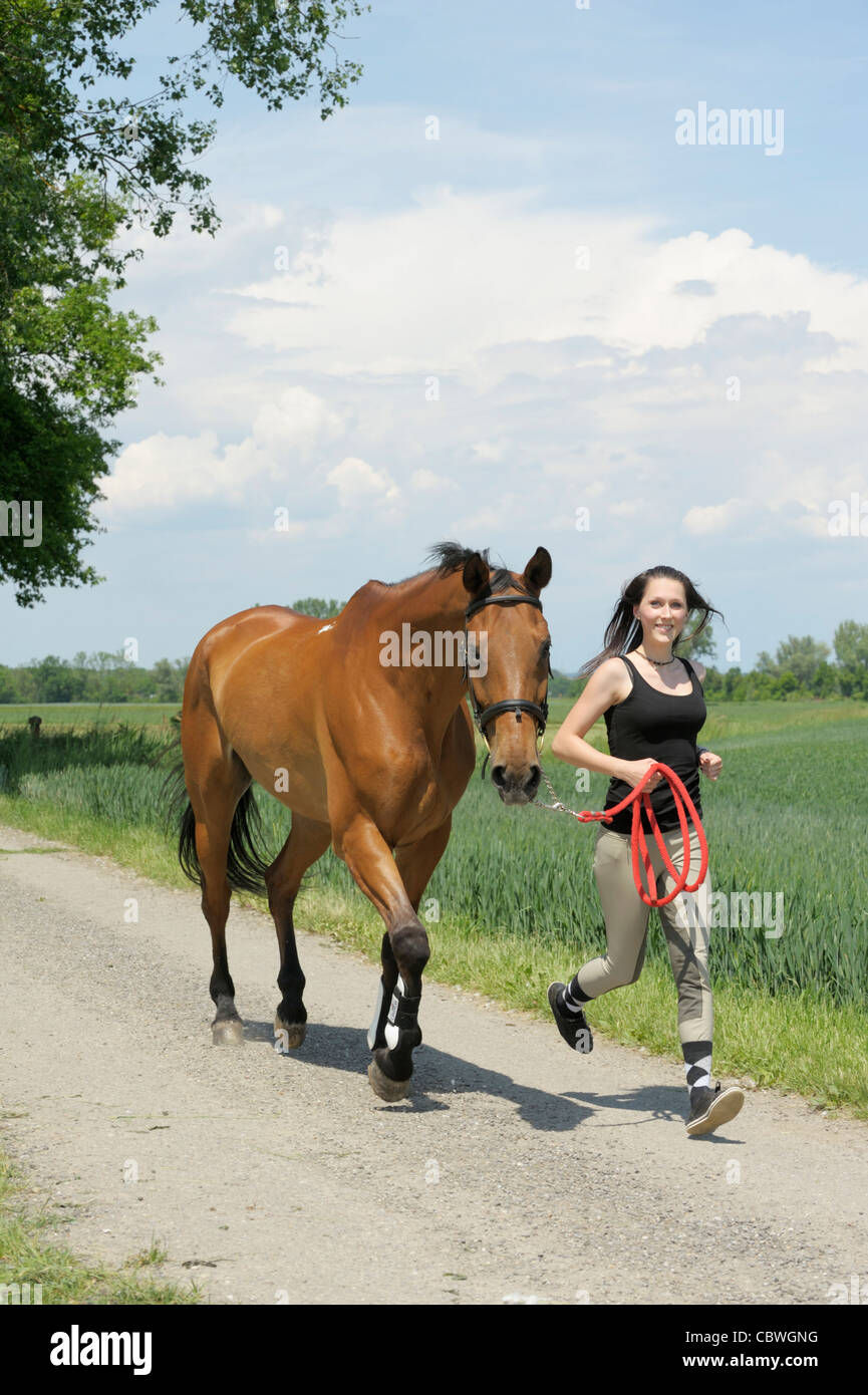 Donna in corsa accanto al suo cavallo trotto Foto Stock