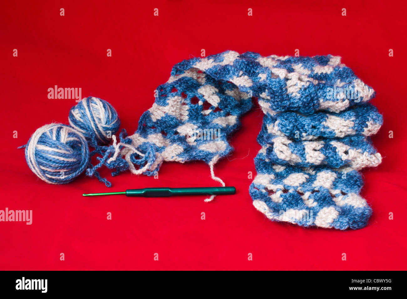 Palla di filati per maglieria e spiedini. Blu e bianco sciarpa a colori su sfondo rosso Foto Stock