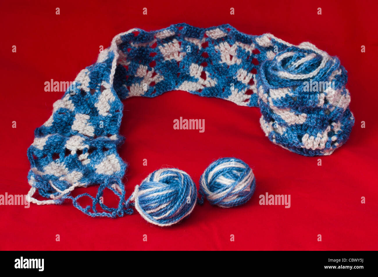 Palla di filati per maglieria e spiedini. Blu e bianco sciarpa a colori su sfondo rosso Foto Stock