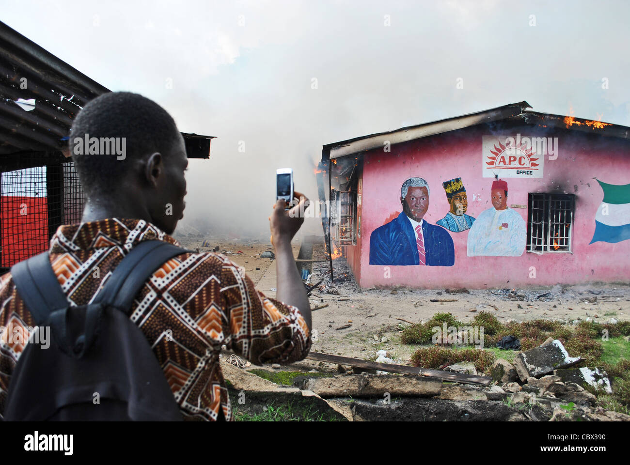 Un uomo che usa il telefono per fotografare la masterizzazione di ufficio dell'APC durante il partito politico (pre-elettorale) violenza, Bo Sierra Leone Foto Stock