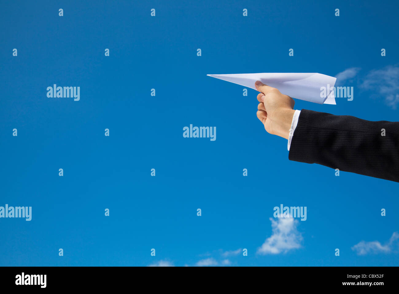 La mano di imprenditore lasciando un aereo fatta di carta volare oltre il cielo blu Foto Stock