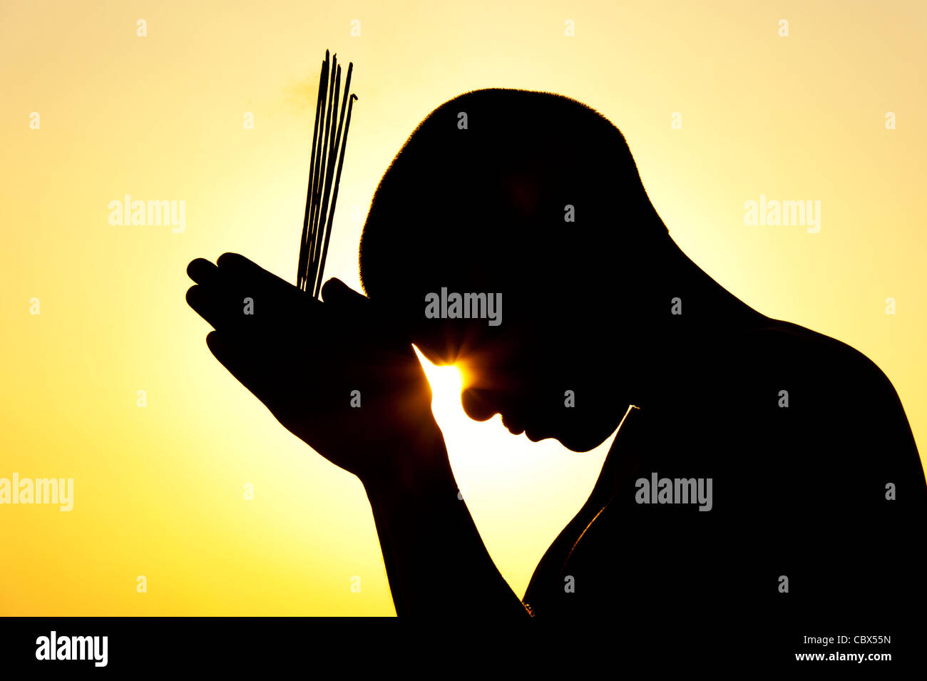 Pregando uomo indiano con bastoncini di incenso al tramonto. Silhouette. India Foto Stock