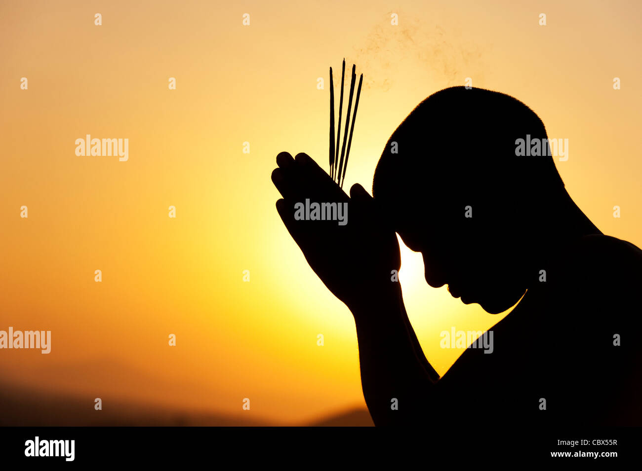 Pregando uomo indiano con bastoncini di incenso al tramonto. Silhouette. India Foto Stock