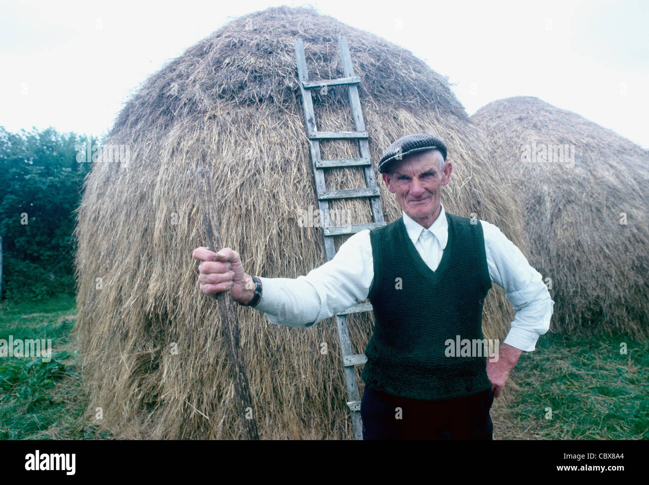 Un agricoltore pone da un fieno rick in Irlanda rurale Foto Stock