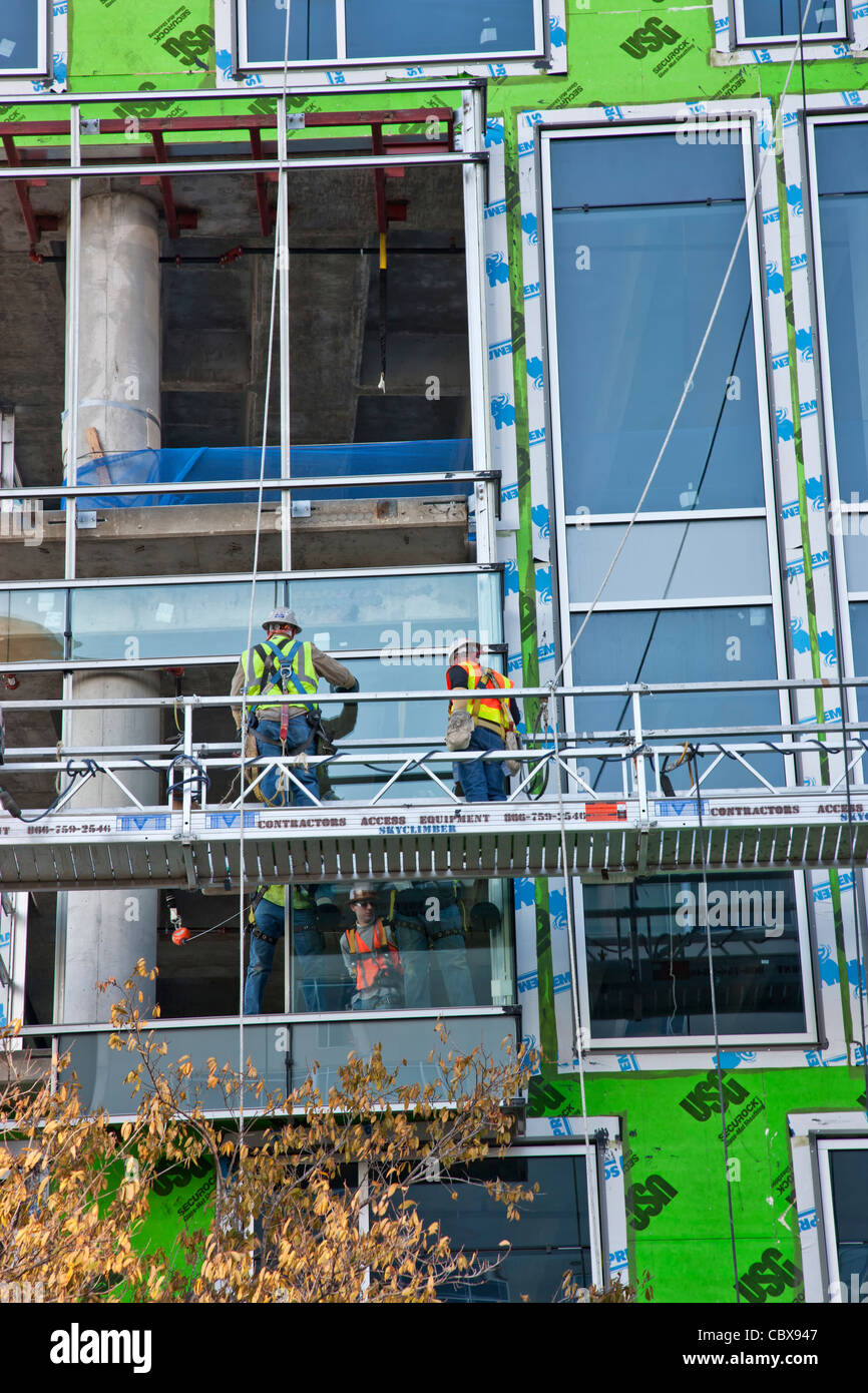 Alto edificio di costruzione, lavoratori installazione di finestre da pavimento a soffitto. Foto Stock