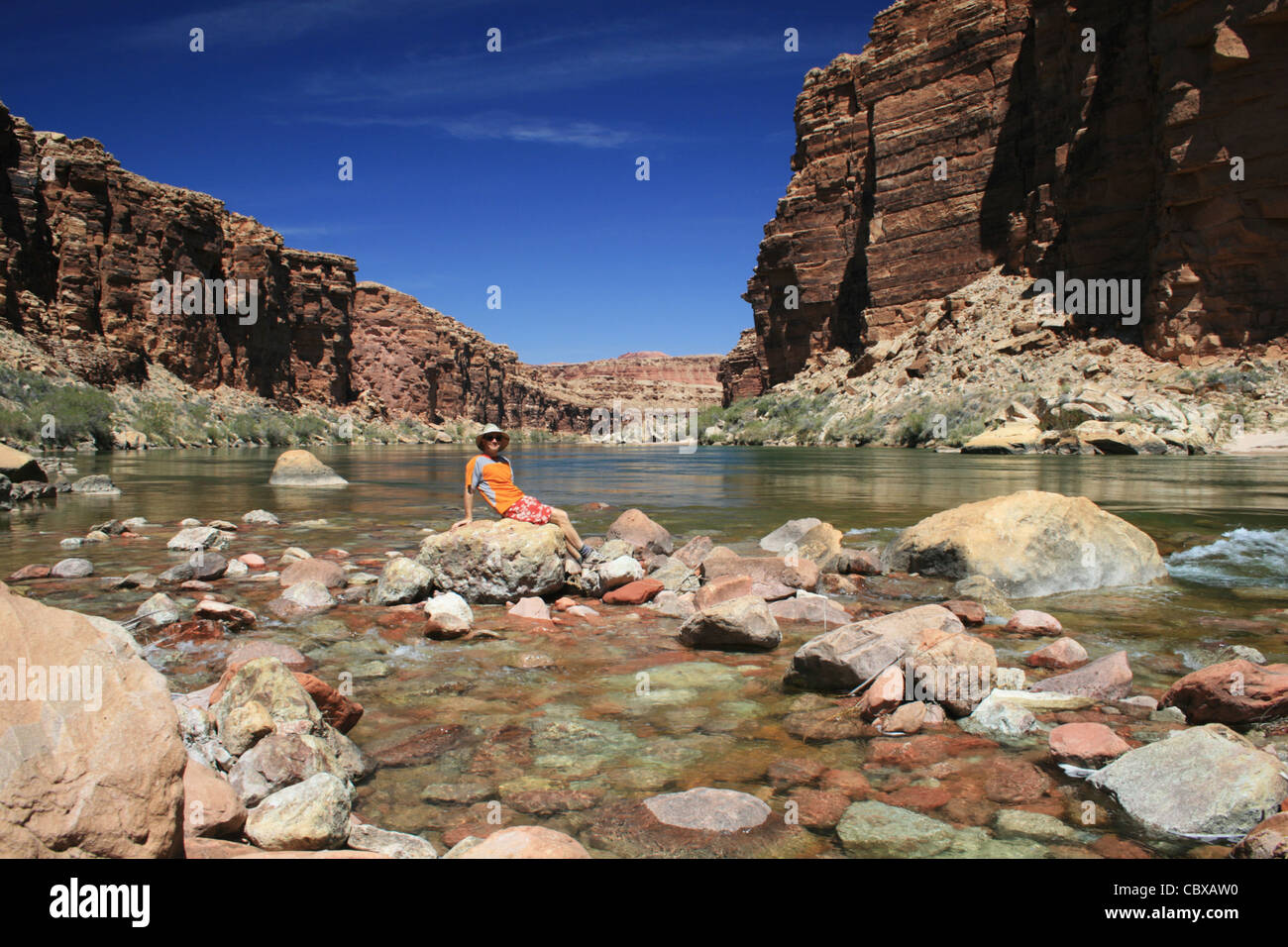 Un uomo in arancione si siede su una roccia nel fiume Colorado in Marble Canyon Foto Stock
