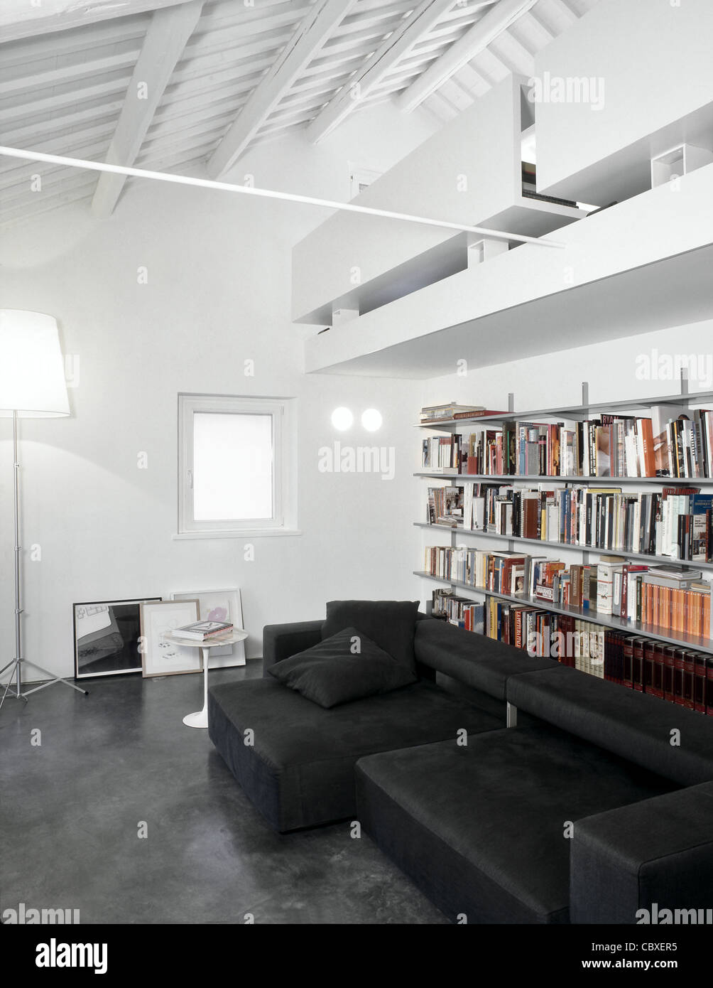 Soggiorno moderno in mansarda con un divano grigio di tessuto e pavimento in resina Foto Stock