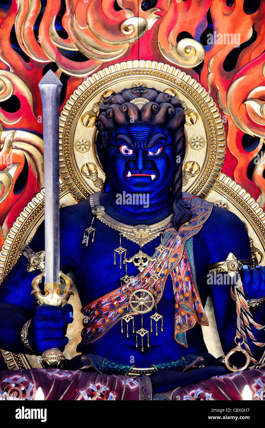Statua di Fudō Myōō Tempio Naritasan Shinshoji Narita Giappone // NARITA, Giappone — l'imponente statua di Fudō myōō (Re della saggezza inamovibile) si trova all'interno del Daitou (grande Pagoda) al tempio Naritasan Shinshoji. Questa figura centrale di culto rappresenta una delle divinità più importanti del buddhismo Shingon, che funge da protettore che rimuove gli ostacoli e distrugge il male. La statua è ospitata all'interno della pagoda alta 58 metri, che è stata costruita nel 1984 come parte della moderna espansione del complesso del tempio. Fudō myōō è tipicamente raffigurato con un'espressione feroce e circondato da fiamme, simboleggiando il bu Foto Stock