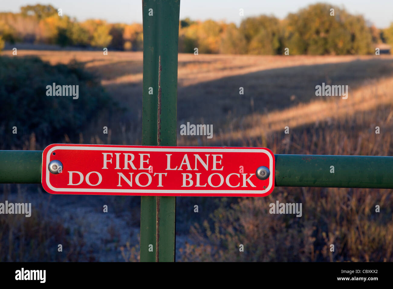 Fire lane non bloccano il segno su un cancello con un prato e bosco paesaggio dietro Foto Stock