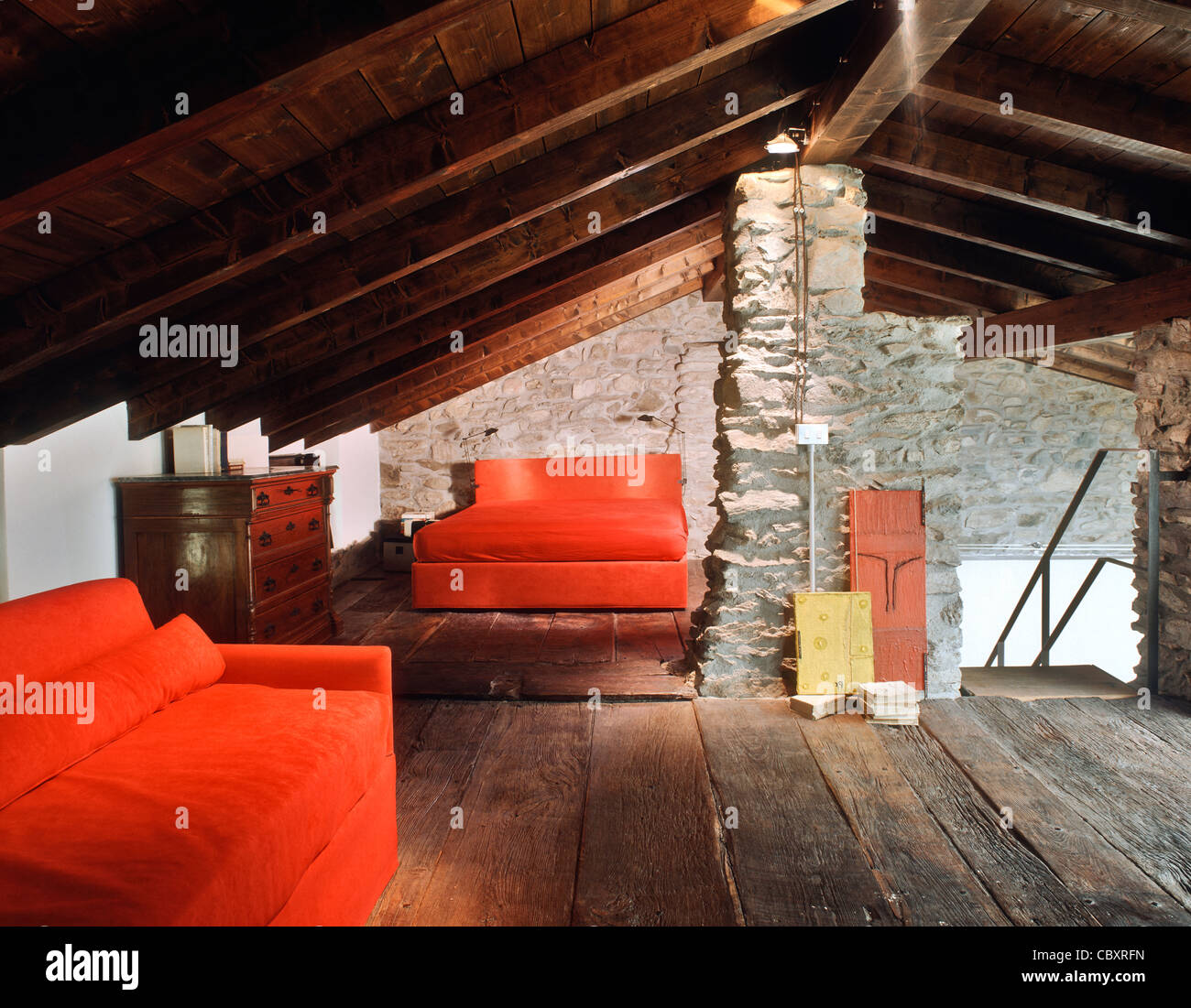 Soppalco con divano letto rosso e le pareti sono di pietra e il pavimento è di legno in una vecchia casa per le vacanze Foto Stock