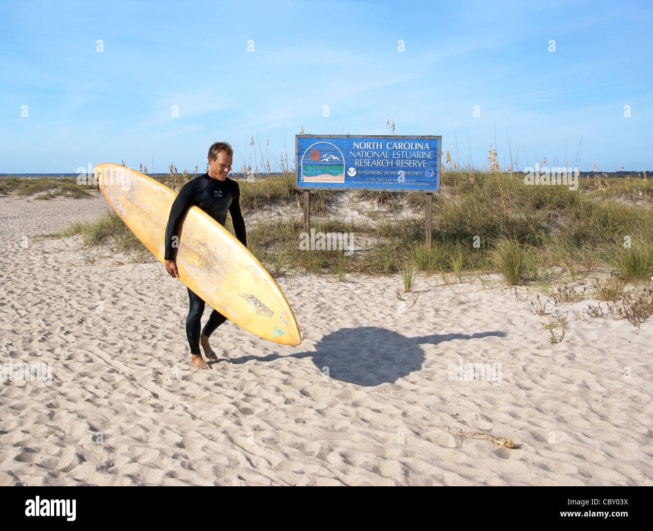 Wrightsville Beach, Wilmington, Carolina del Nord, NC. Un surfista passeggiate passato un segno di informazioni. Foto Stock